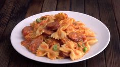 a white plate topped with pasta covered in sauce and meat toppings on top of a wooden table