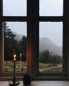 a candle sitting on top of a window sill next to a cup and mug