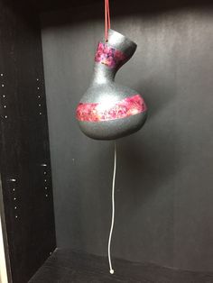 a gray vase with pink and red designs hanging from it's side on a black shelf