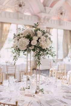 a tall vase filled with white flowers sitting on top of a table covered in gold chairs