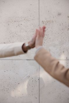 two people reaching out their hands towards each other in front of a white tiled wall