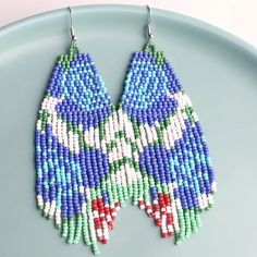 two pairs of beaded earrings are sitting on a blue plate with white and green beads