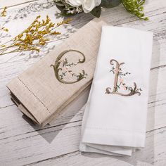 two napkins with embroidered letters on them sitting next to each other and flowers in the background