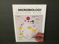 the microbiology coloring book is being held up by someone's hand and pointing at it