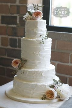 a three tiered cake with flowers on the top is sitting on a table in front of a brick wall