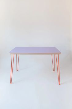 a purple table with orange legs on a white background in front of a pink wall