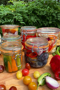 several jars filled with different types of food on a table next to vegetables and fruit