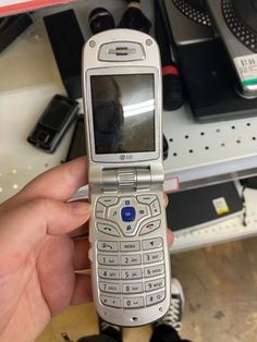 a person holding up a cell phone in their hand with other electronics on the shelf behind them