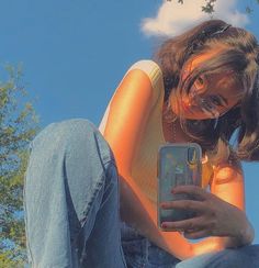 a woman sitting on the ground looking at her cell phone while wearing jeans and a yellow shirt