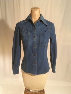 "vintage 1970s women's western denim shirt Brittania Sportswear cotton blue jean button up front 2 bust pockets long sleeve/button cuff yoke hem good vintage condition, light wear labeled size 5, very petite, see below measures, lying flat, shoulder-  13 1/2\" sleeve-20 1/2\" chest-16\" waist-14\" hem-16\" length from top at neck seam below collar-22\"" Fitted Vintage Button-up Denim Top, Western Style Denim Blue Cotton Tops, Denim Blue Button-up Top For Rodeo, Fitted Collared Denim Jacket In Denim Blue, Fitted Collared Denim Jacket With Button Closure, Fitted Collared Denim Jacket With Buttons, Western Style Relaxed Fit Button-up Tops, Classic Fitted Denim Top With Pockets, Classic Fitted Denim Top