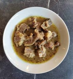 a white bowl filled with meat and gravy on top of a black table