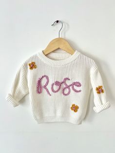 a white sweater with the word rose written on it and flowers in pink, yellow and purple