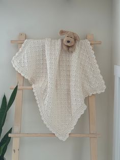 a teddy bear is sitting on top of a crocheted blanket that is draped over a ladder