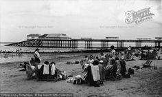 an old black and white photo of people sitting on the beach in front of a pier