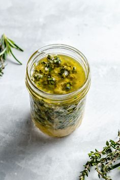 a jar filled with pesto sauce next to some herbs