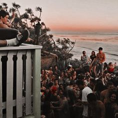 a group of people standing on top of a beach next to the ocean at sunset