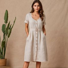 a woman standing in front of a potted plant wearing a white dress with buttons