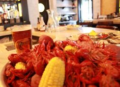 a bowl full of crawfish and corn on the cob next to a glass of beer