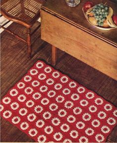 a crocheted rug on the floor in front of a table with fruit and silverware