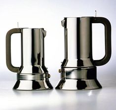 two stainless steel mugs sitting next to each other on a white table with a gray background