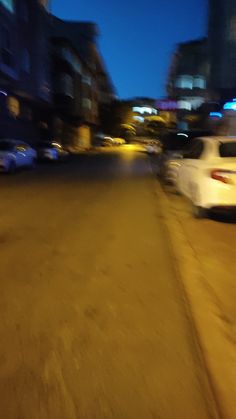 a blurry photo of cars parked on the side of a city street at night