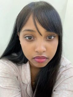 a woman with long black hair wearing a white shirt and pink lipstick looks at the camera