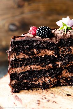 a piece of chocolate cake with raspberries and blackberries on top is sitting on a wooden table