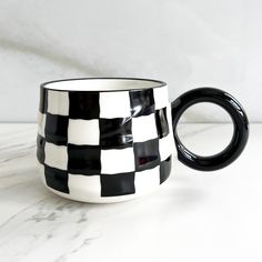 a black and white checkered coffee mug sitting on a marble counter top with the handle extended