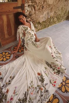 a woman is sitting on the floor in a long white dress with floral embroiderys