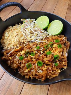 a pan filled with rice and vegetables on top of a wooden table next to two lime wedges