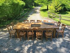 a wooden table and chairs sitting on top of a gravel road next to a forest