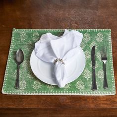 a place setting with napkins and silverware on a green place mat, along with a fork and knife