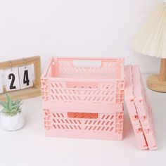 a pink crate sitting on top of a white table next to a clock and plant