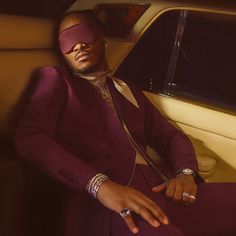 a man in a purple suit and blindfolded headgear sitting in a car