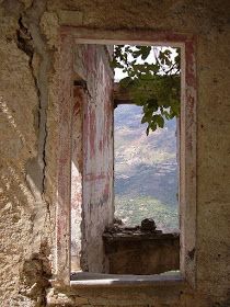 an open window in the side of a stone building with a view of a valley