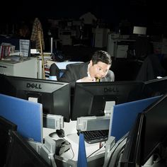 a man sitting in front of two computer monitors on top of desks with computers behind him