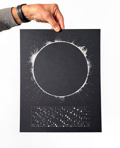 a person holding up a black paper with white dots in the shape of a circle