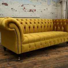 a yellow couch sitting on top of a wooden floor next to a white brick wall