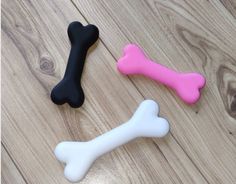 three different colored bone shaped toys on a wooden floor, one black and one pink