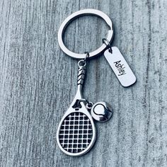 a tennis racquet and ball keychain on a wooden surface with a tag