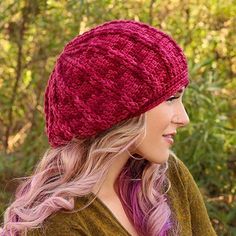 a woman with pink hair wearing a red knitted hat in front of some trees