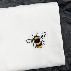 a white t - shirt with a yellow and black bee embroidered on it