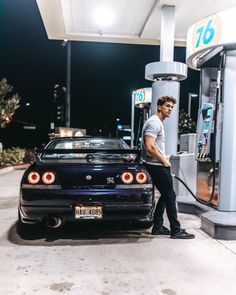 a man filling up his car with gas at a gas station in front of a gas pump