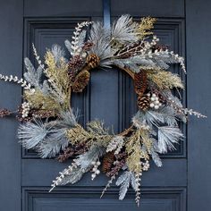 a wreath with pine cones and evergreen needles is hanging on the front door's blue painted panel