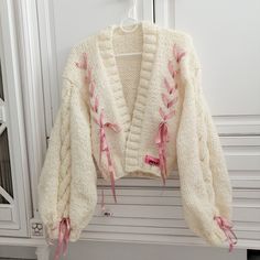 a white sweater with pink laces hanging on a door handle in front of a cabinet