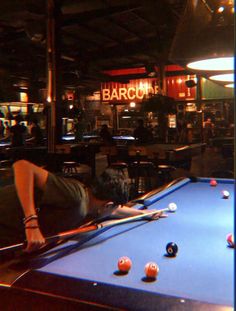 a man laying on top of a pool table next to a blue billiarde