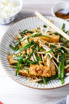 a white plate topped with tofu, green beans and rice next to chopsticks