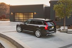 a black volvo suv is parked in front of a modern house at sunset or dawn