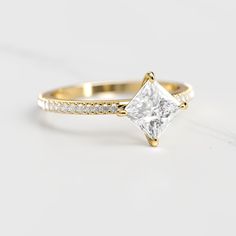 a gold engagement ring with a princess cut diamond and pave set diamonds on the band