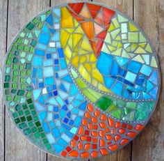 a colorful mosaic glass plate sitting on top of a wooden table next to a wall